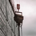 A crane lifting a concrete container at a construction site against a cloudy sky.