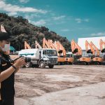 A photographer takes photos at a construction site with heavy machinery and trucks on a sunny day.
